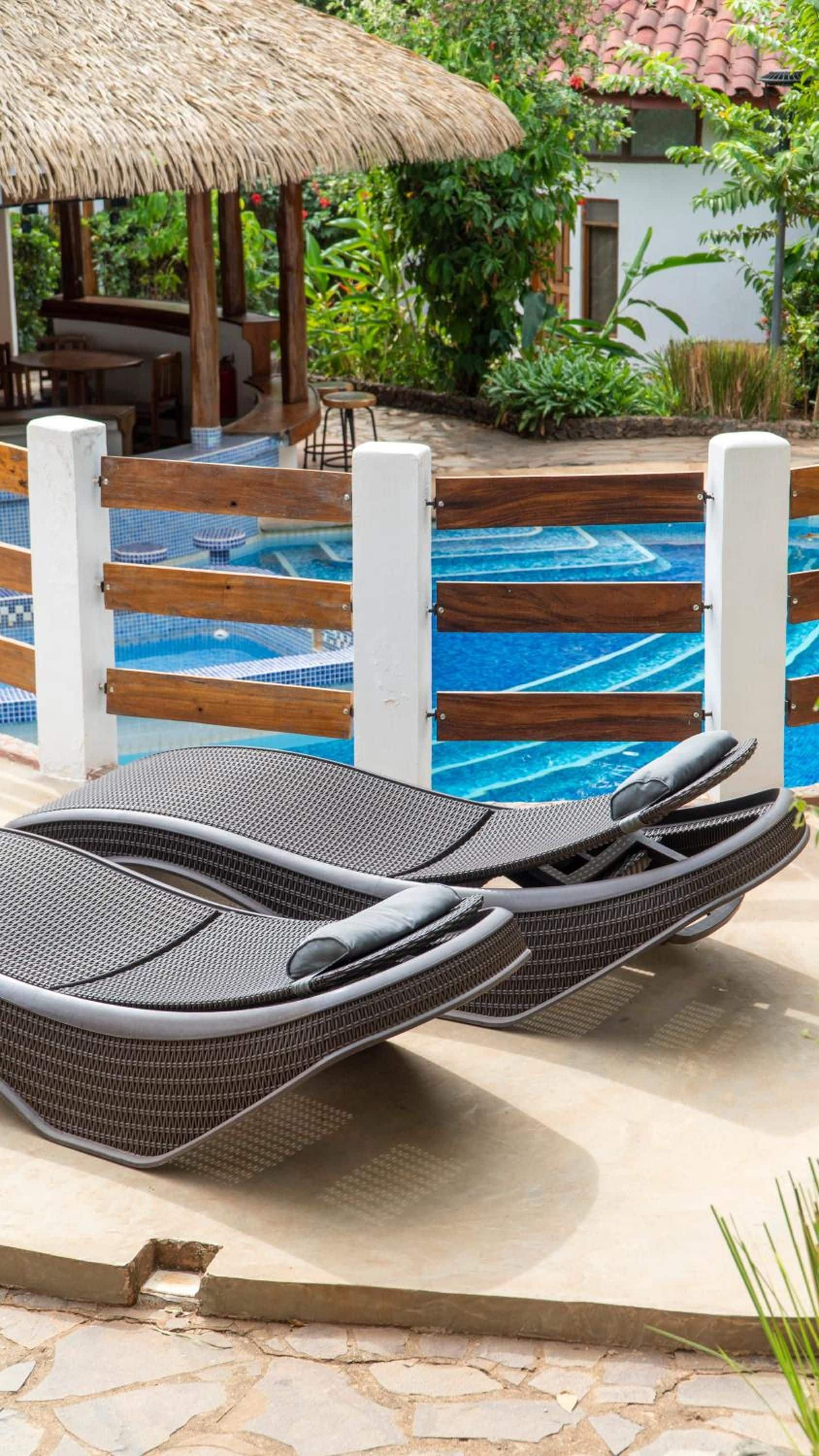 A poolside area with a lounge chair, a thatched roof structure, and a pool with blue tiles.