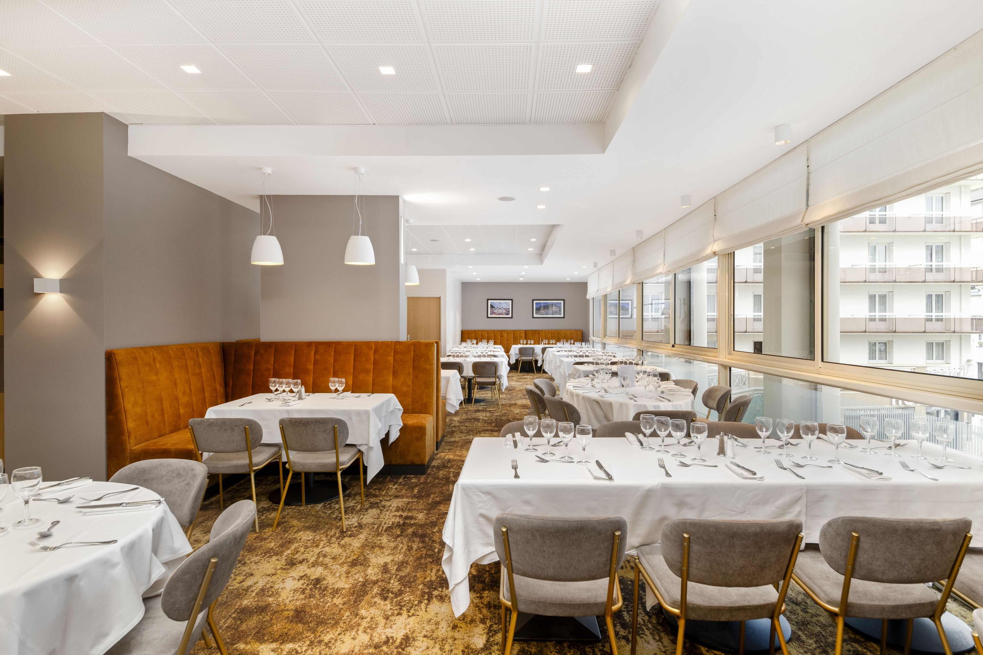 Un restaurant doté de nombreuses tables, de coins salons et offrant une vue sur la ville grâce à de grandes fenêtres.