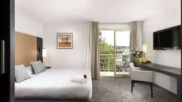 A hotel room with a bed, a desk, a chair, a TV, and a balcony with a view.