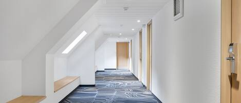 Un pasillo moderno con alfombra estampada, paredes blancas y bancos de madera.