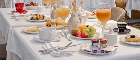 Un bufé de desayuno con diversos pasteles, frutas y bebidas sobre un mantel blanco.