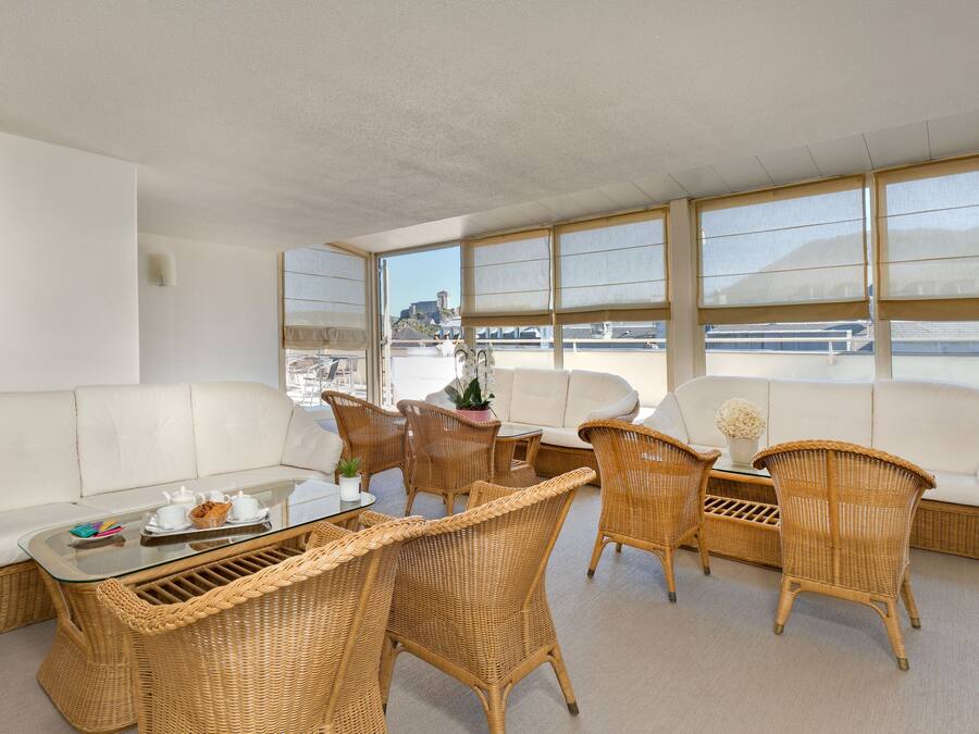 A sunlit room with a white sofa, wicker chairs, and a glass coffee table.