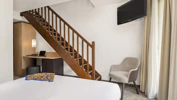 Een hotelkamer met een houten trap, een flatscreen televisie aan de muur, een bureau met een lamp, een stoel en een bed.