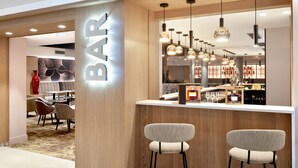 Eine moderne Bar mit Holzakzenten, hängenden Pendelleuchten und einer Bar Theke mit Hockstühlen.