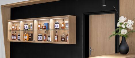 Zona de recepción con un mostrador de madera, una puerta negra y una estantería que exhibe diversas botellas de licor.