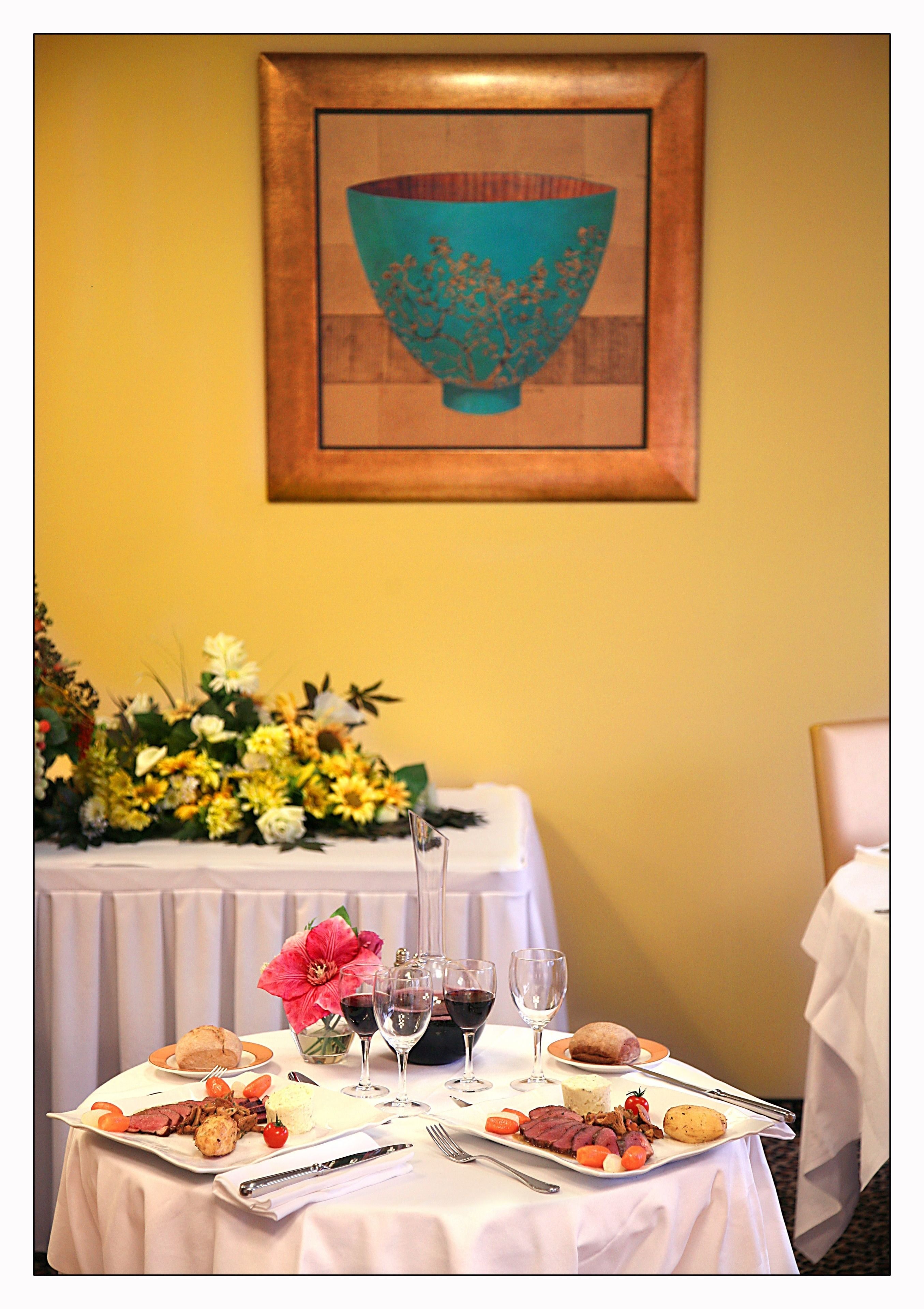 Una mesa de comedor dispuesta con comida, copas de vino y un centro de mesa floral.
