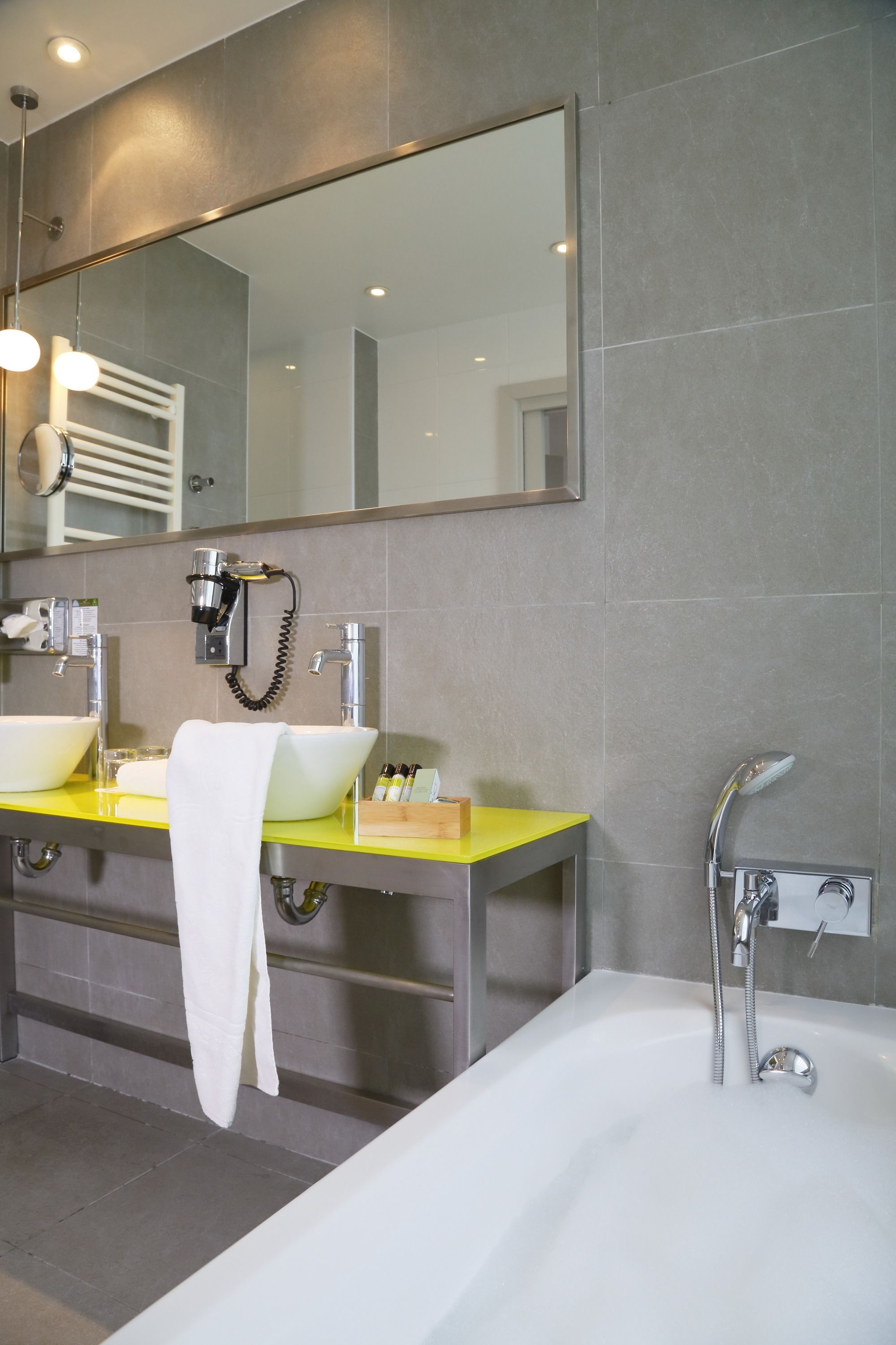 A modern bathroom with a large mirror, two sinks, a bathtub, and a towel hanging on the wall.