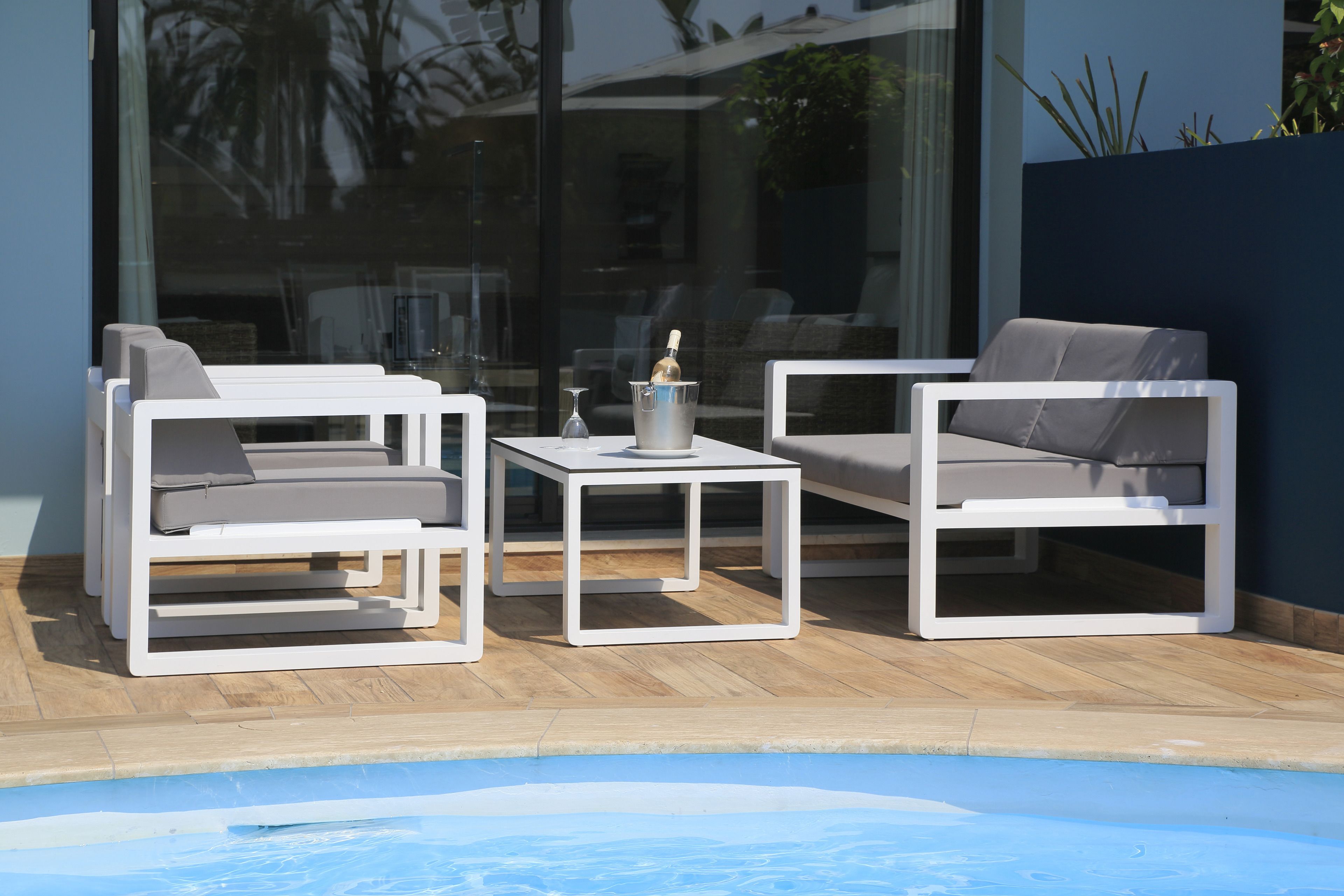 A poolside area with two white lounge chairs and a small table, each with a cushion.