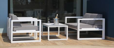 A poolside area with two white lounge chairs and a small table, each with a cushion.