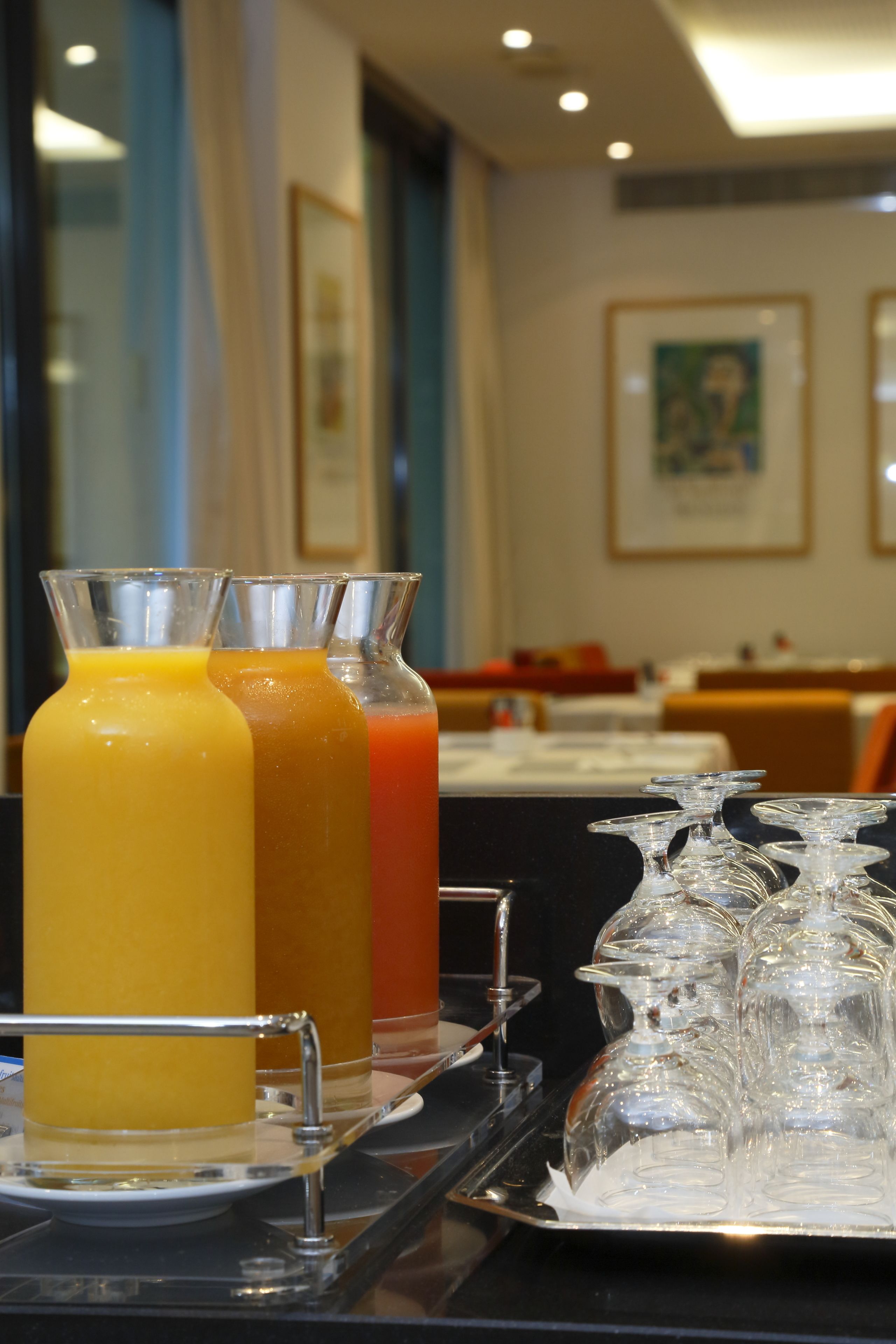 A breakfast bar with three juice dispensers and a tray of clear glassware.