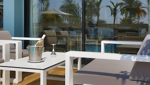 A modern outdoor seating area with white furniture, a glass table, and a view of palm trees and a pool. - Hotel Napoleon (Menton)
