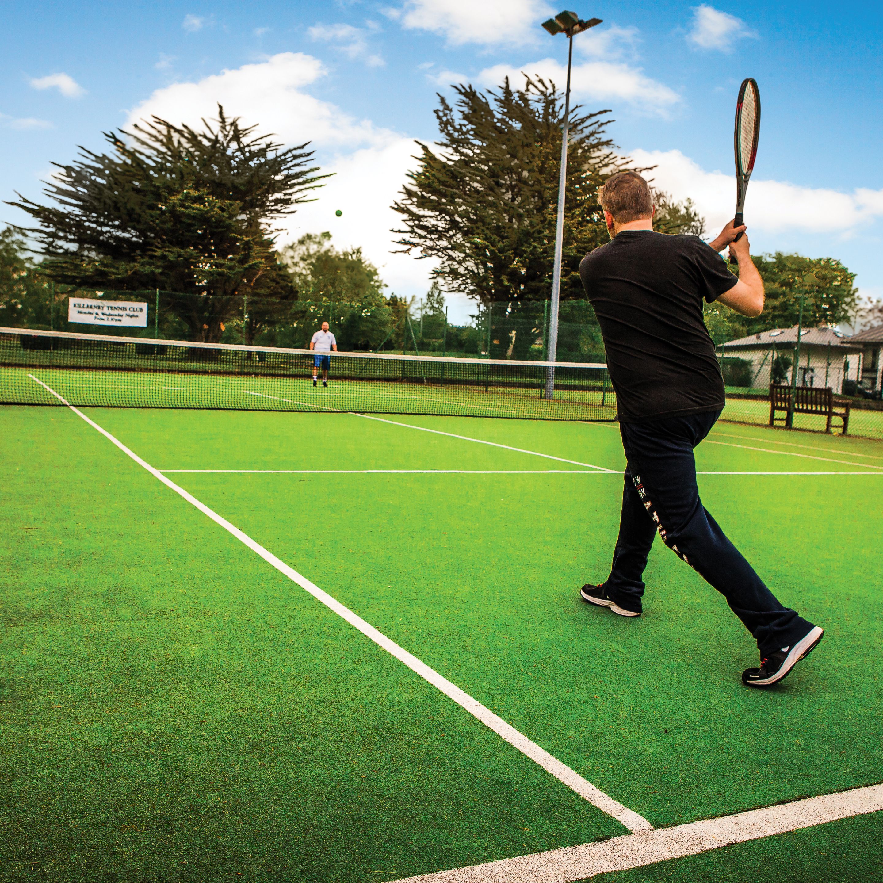 A tennis court with a net, a player in black, and a sign in the background.