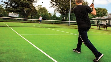 A tennis court with a net, a player in black, and a sign in the background.
