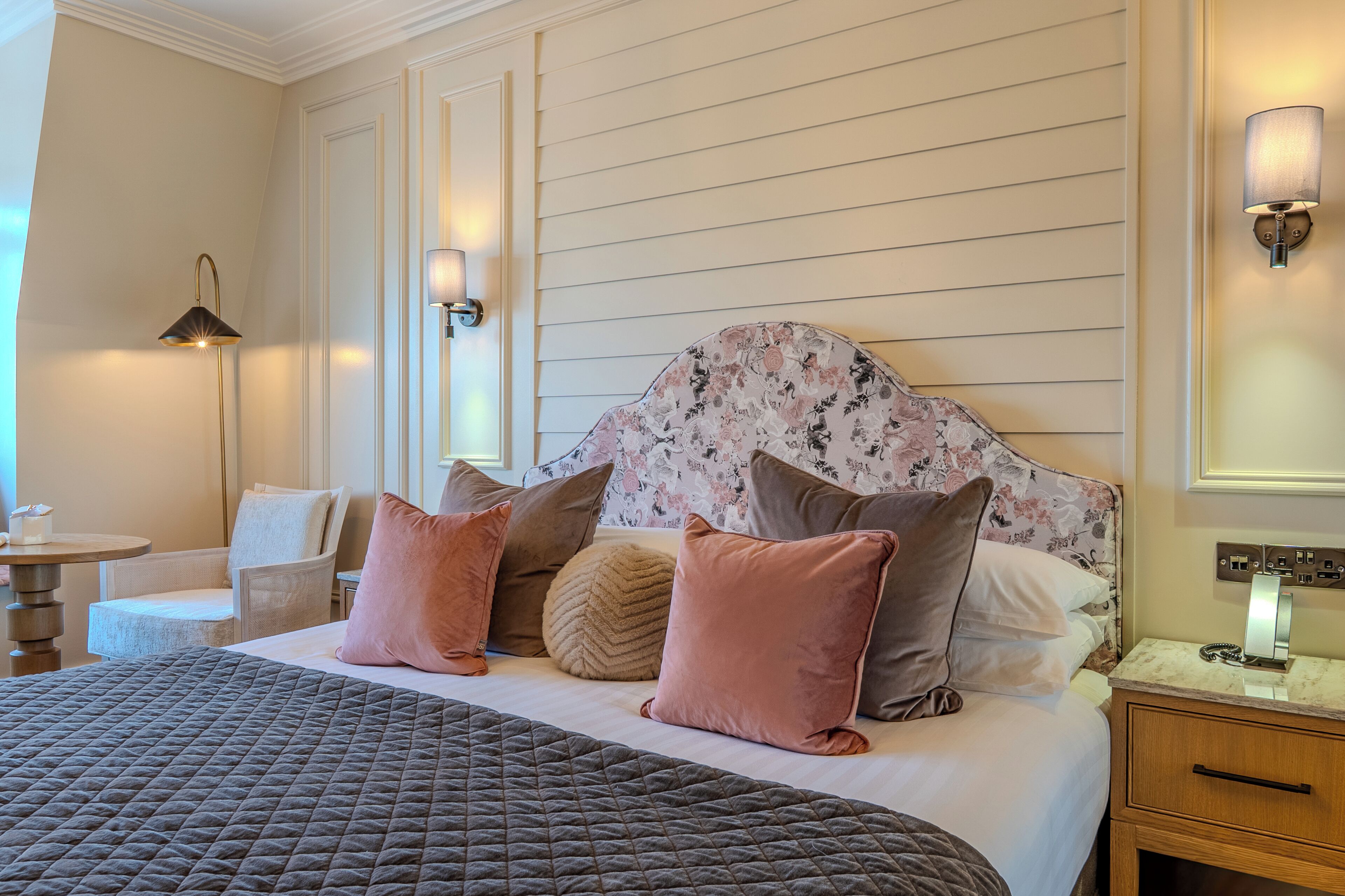 A neatly arranged hotel room with a bed, bedside table, lamp, and a chair.