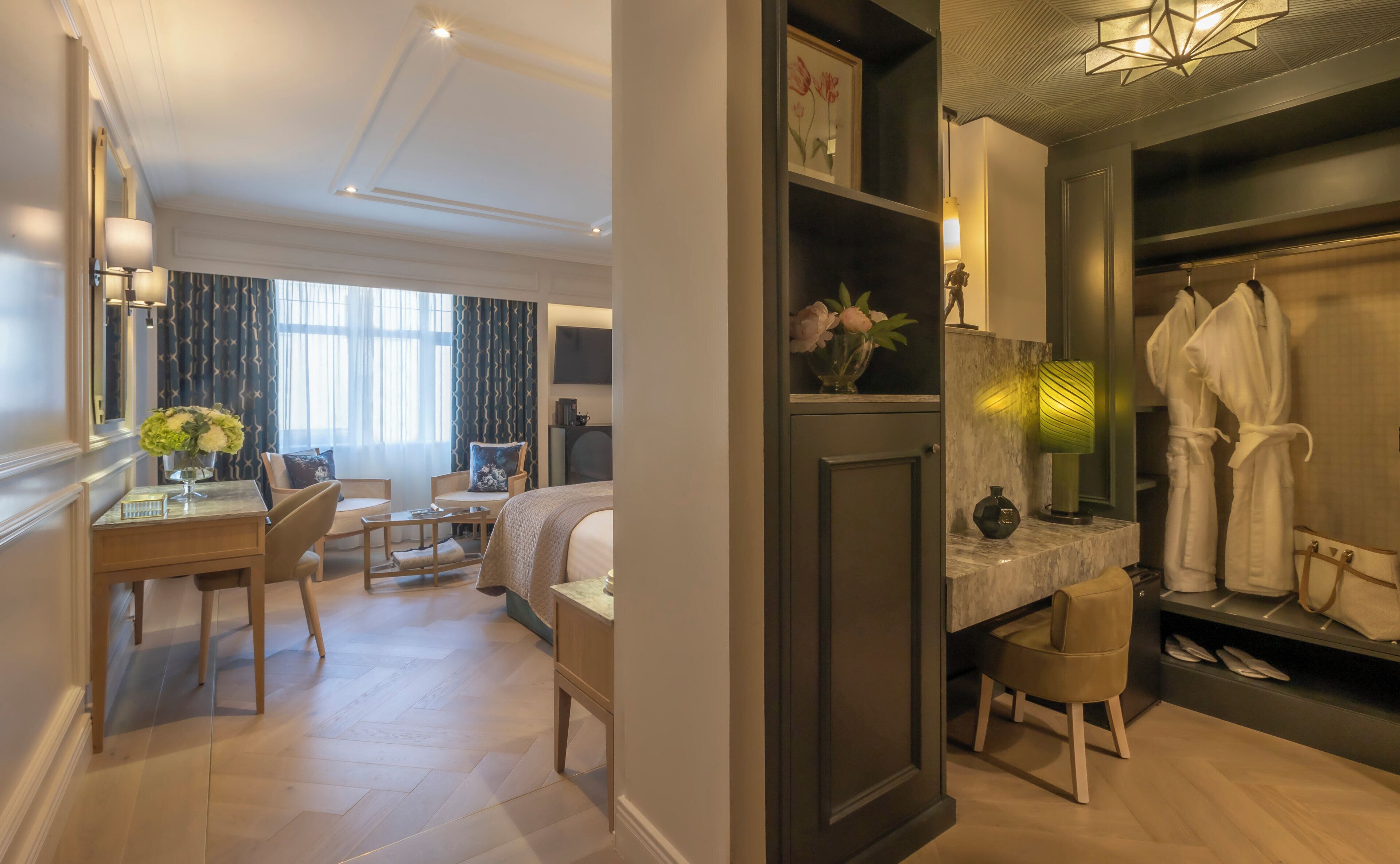 A hotel room with a bed, a desk with a chair, a vanity with a mirror, and a robe rack.