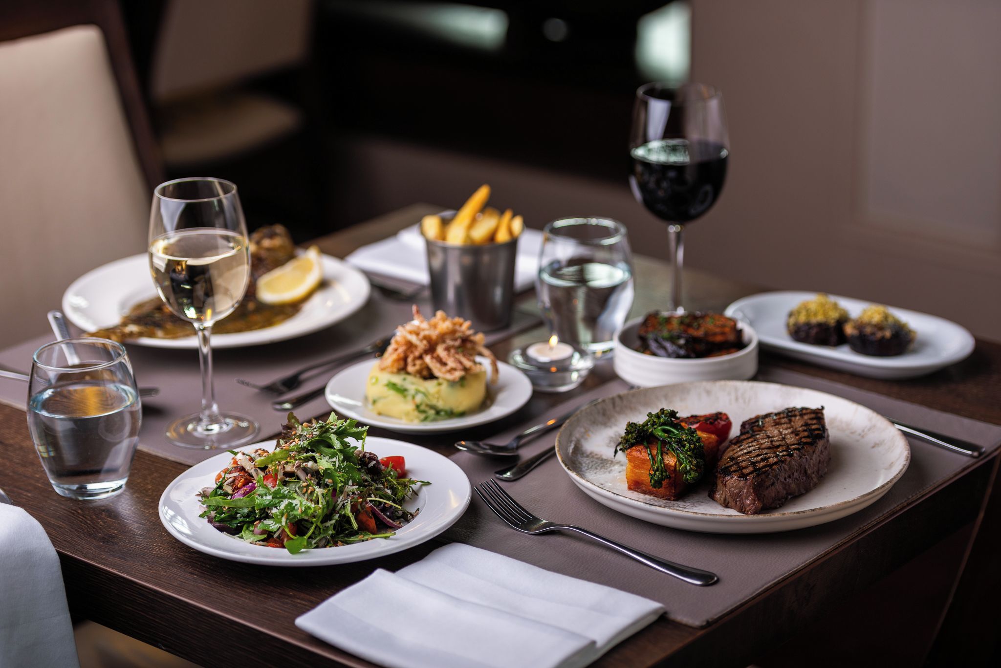 Une table à manger avec différents plats, des verres d’eau et de vin, ainsi que des couverts.