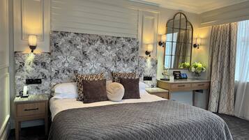Habitación de hotel con una cama grande, una mesita de noche, un aparador, un espejo y una ventana con cortinas.