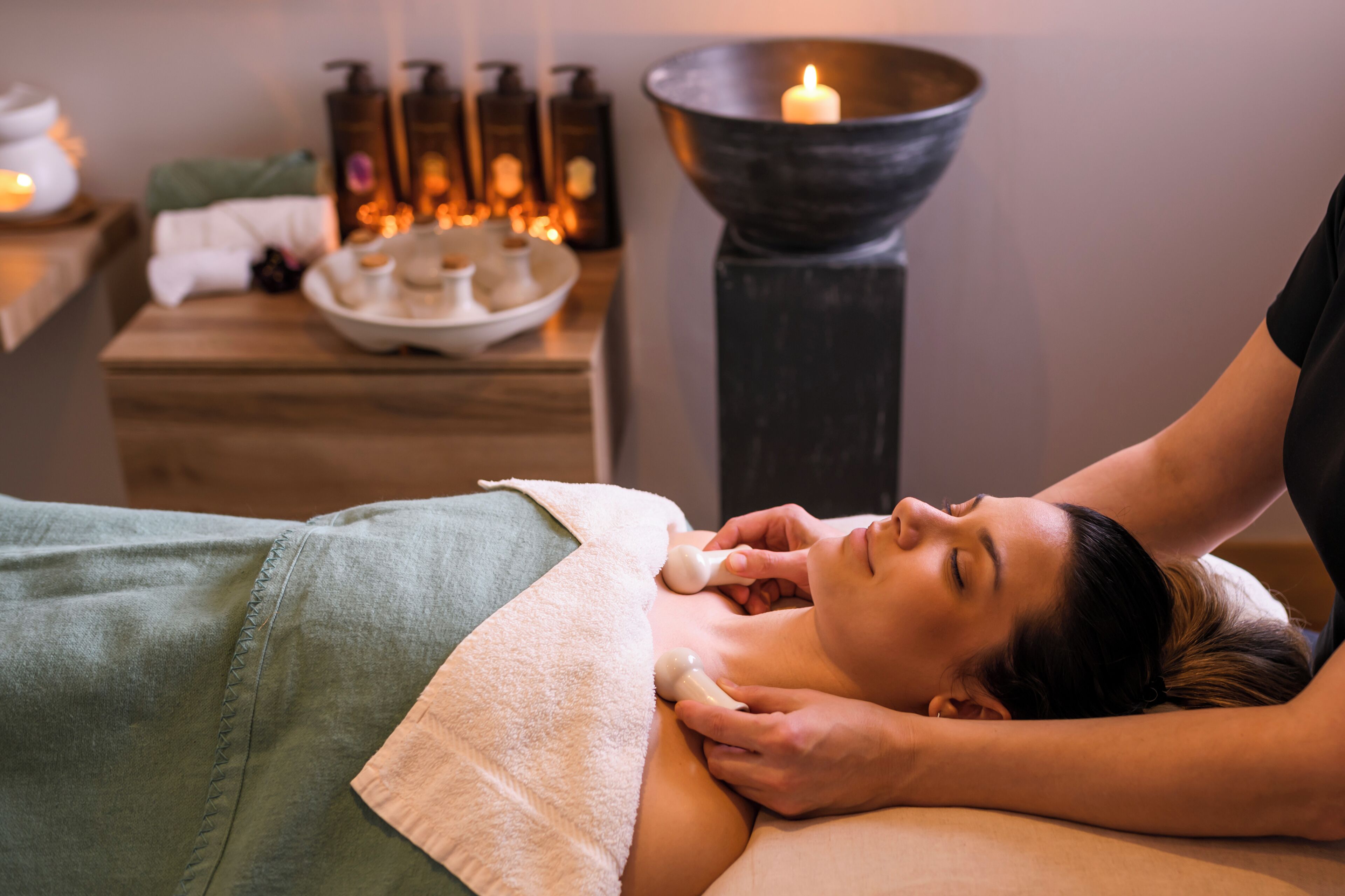 A massage therapy session in a spa setting with a wooden table, candles, and essential oil bottles.