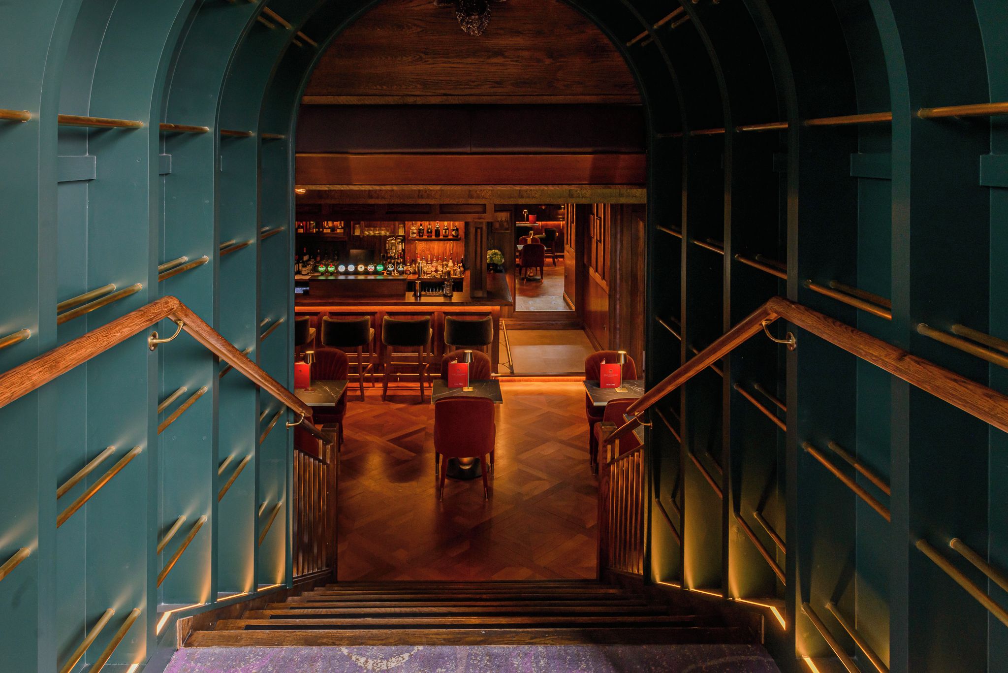 Una escalera conduce a un área de bar con barandillas de madera y una barra.