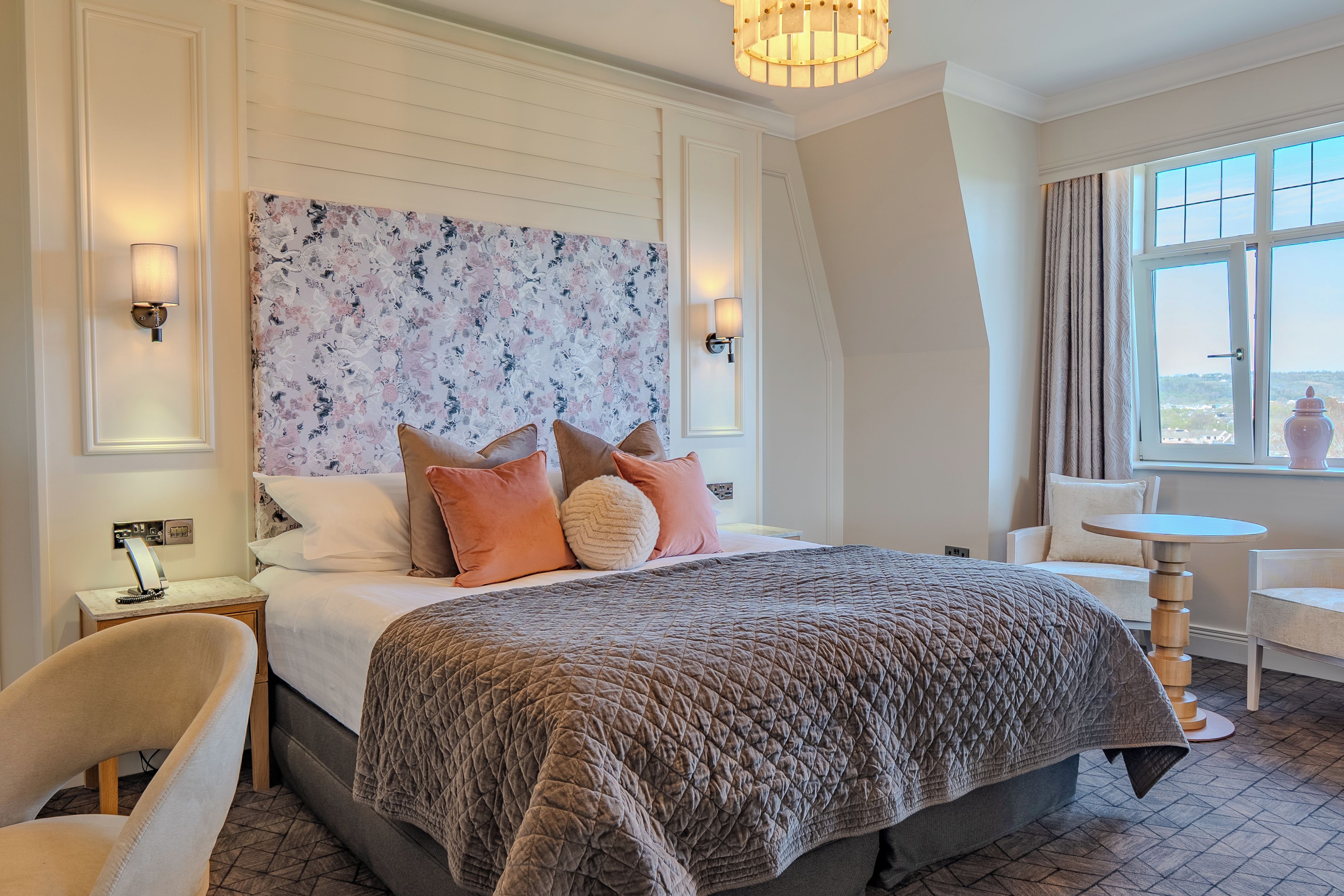 A hotel room with a large bed, a desk, a chair, and a view of the city through the window.
