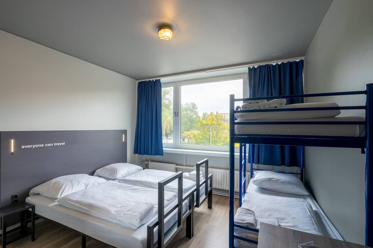 Ein Schlafsaalzimmer mit Etagenbetten, einem Schreibtisch, einem Stuhl und einem Fenster mit Vorhängen.