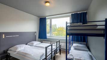 A dormitory room with bunk beds, a desk, a chair, and a window with curtains.