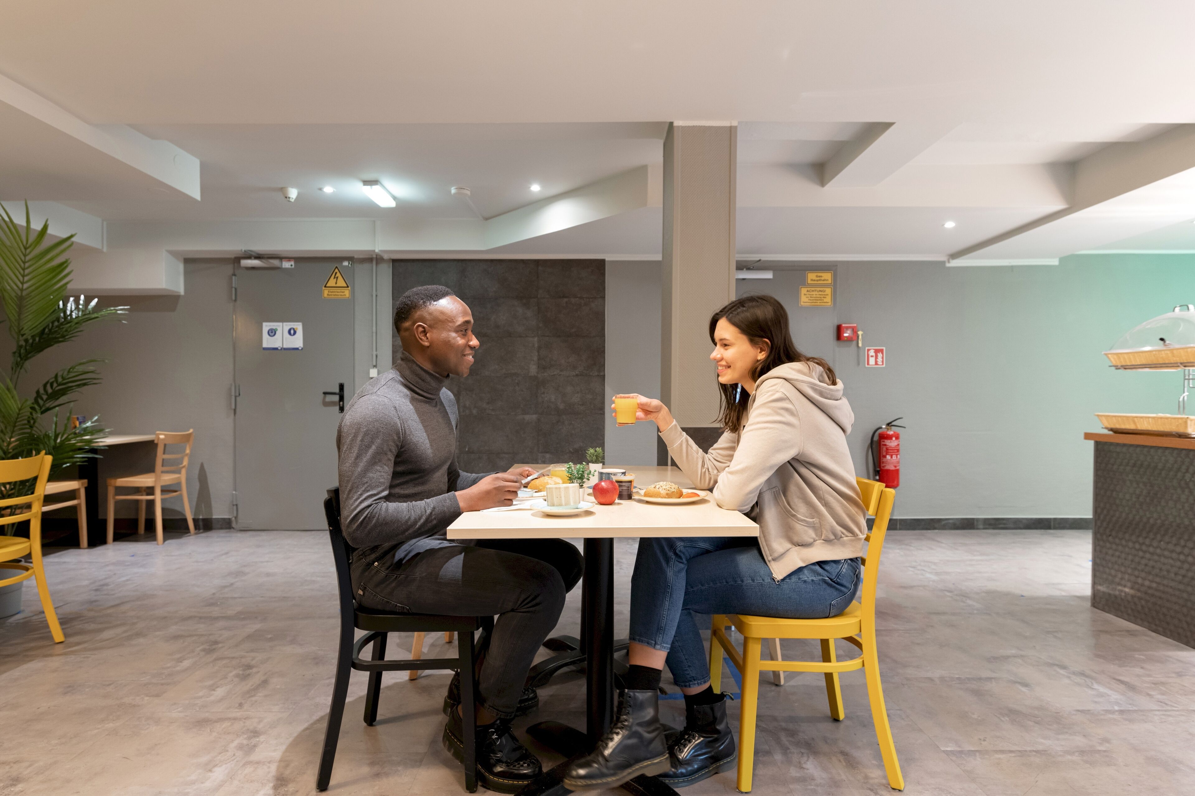 A modern dining area with a table set for two, chairs, and a small plant.