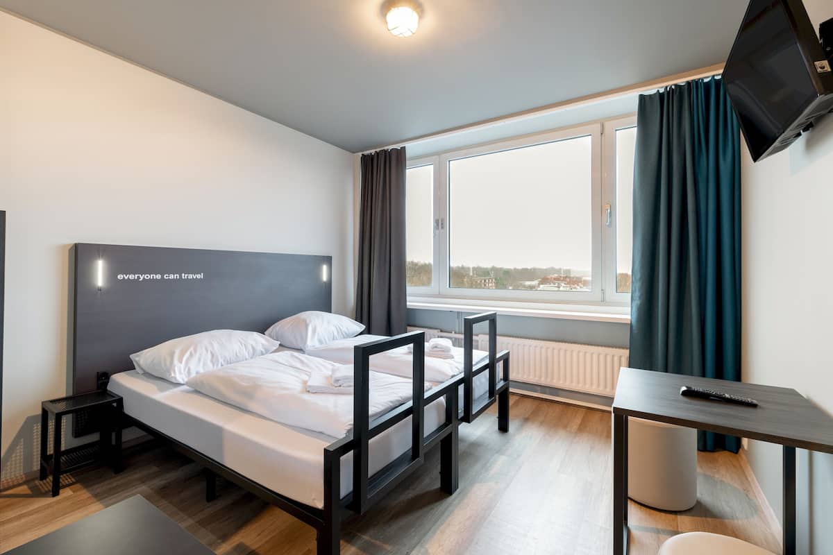 Ein modernes Hotelzimmer mit Bett, Schreibtisch, Fernseher und einem Fenster mit Vorhängen.
