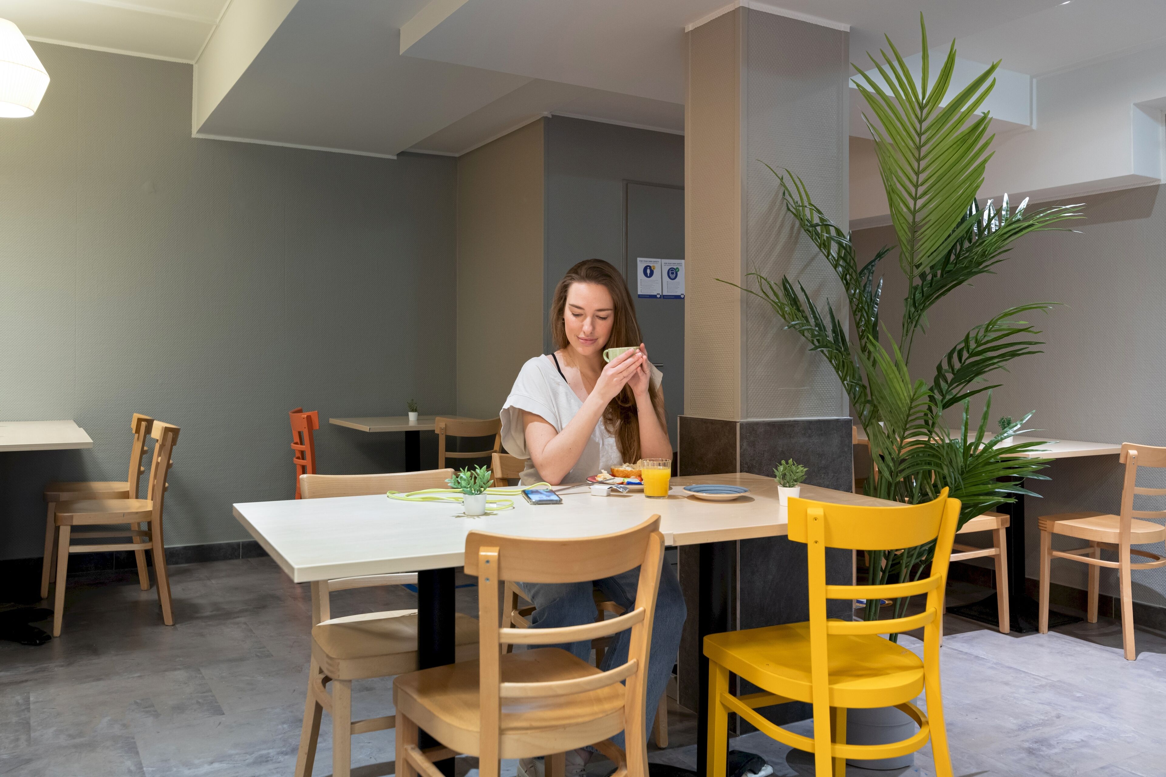 A person sitting at a table with a plant, a glass of orange juice, and a smartphone.
