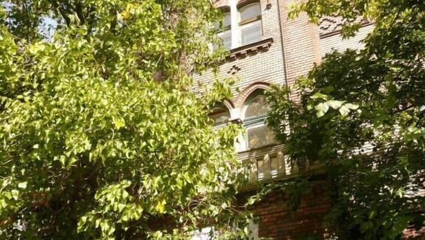 Een hotelschiltje met de naam 'Dominik Panzio' voor een bakstenen gebouw met boogvensters en een toren.
