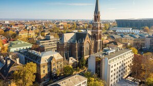 Stadsgezicht met een opvallende kerk, herkenbaar aan een hoge spits en gedetailleerde architectuur, omringd door een combinatie van moderne en oudere gebouwen.