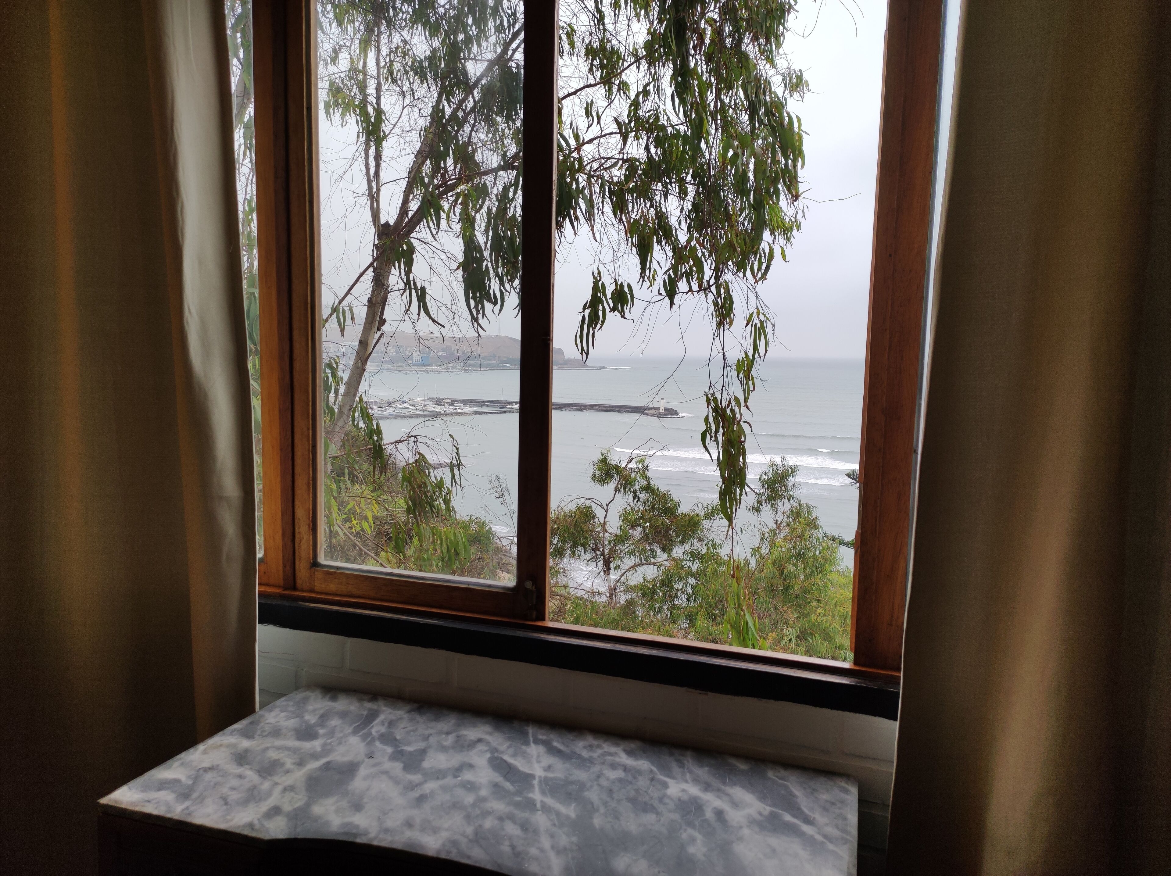 A room with a view of the ocean through a window with curtains.