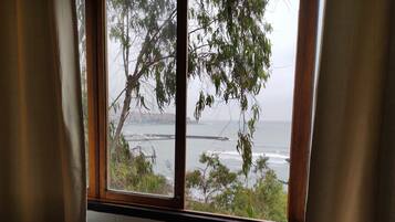 A room with a view of the ocean through a window with curtains.