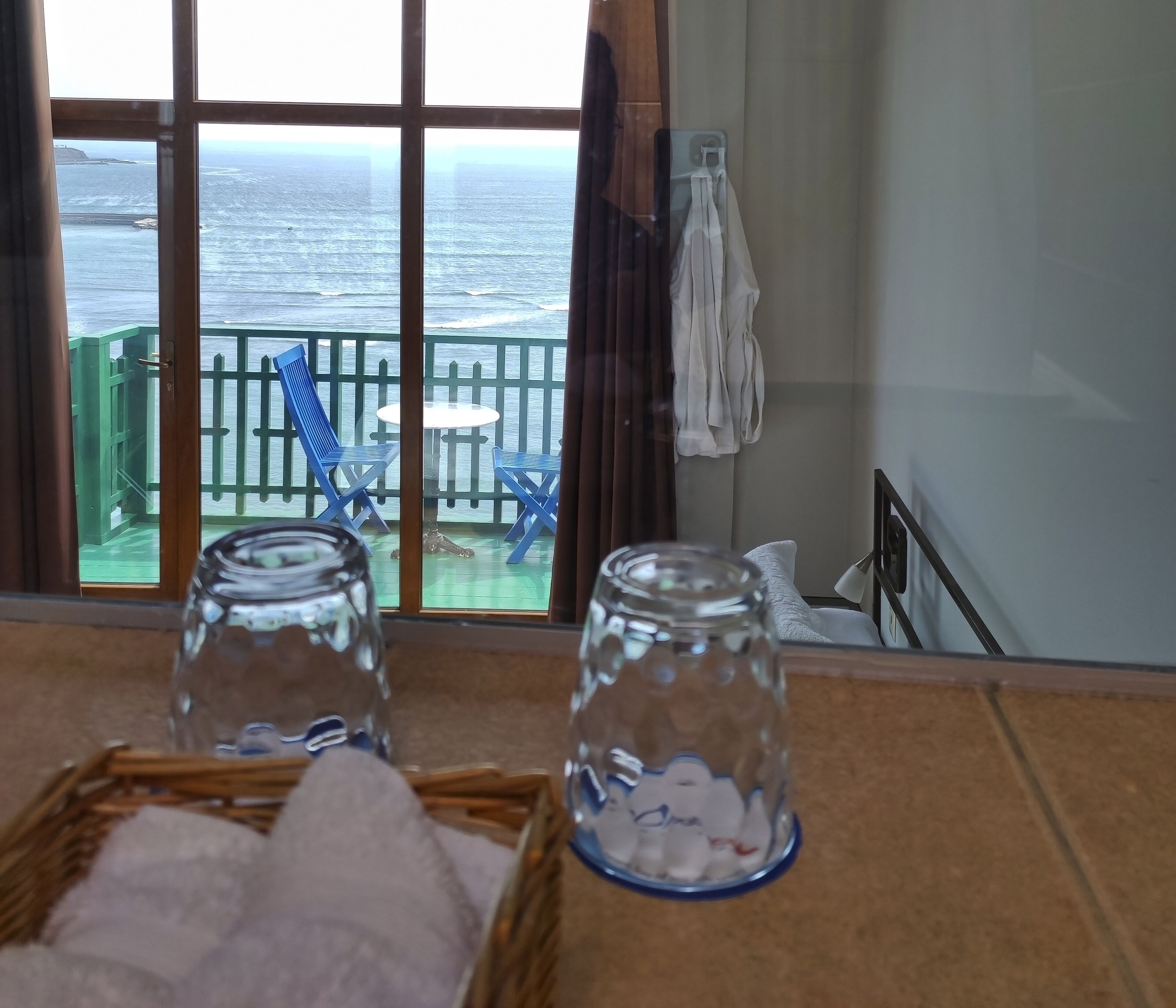 A room with a view of the sea through large windows, a table with a basket of towels, and two glass jars with items inside.
