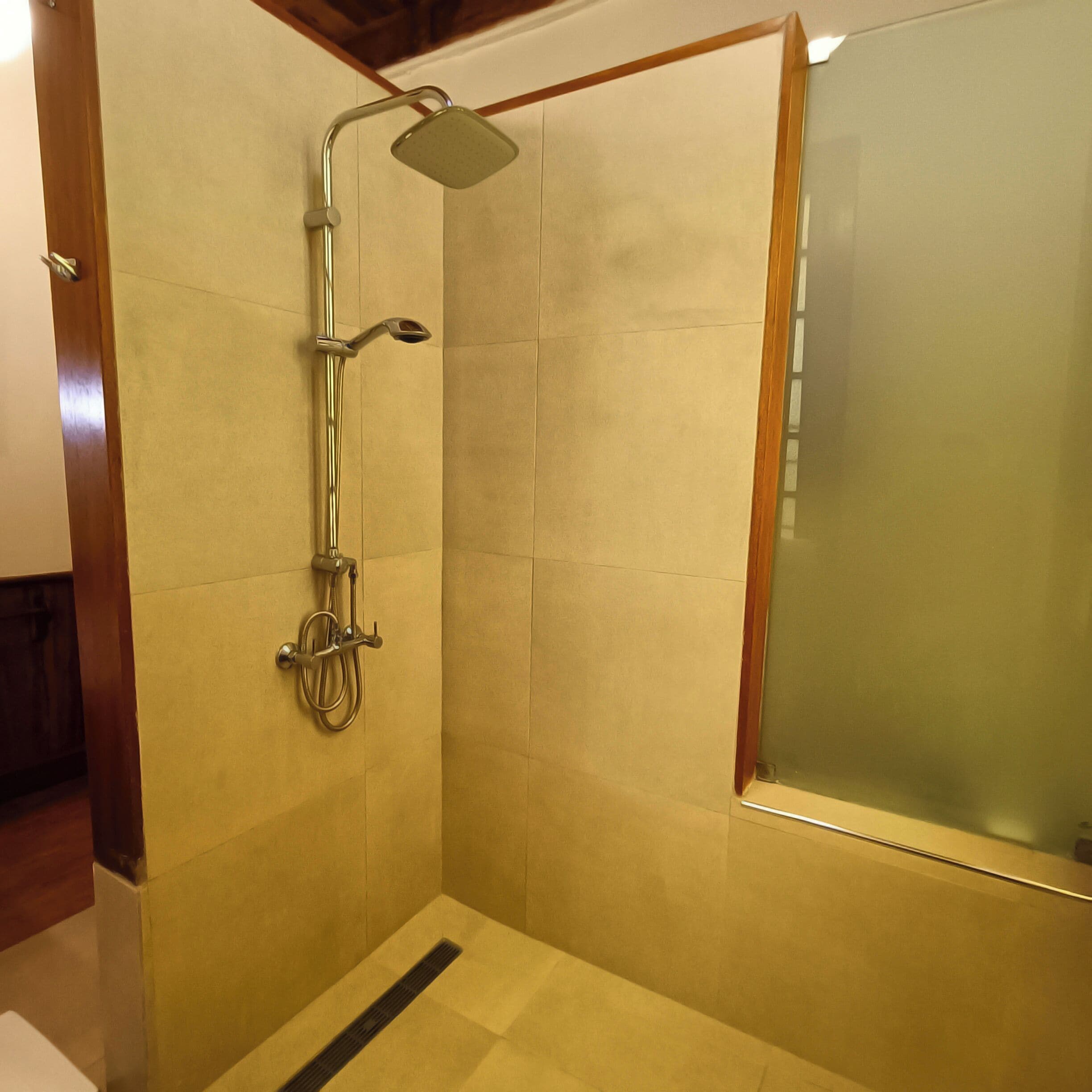 A shower with a glass door, a handheld showerhead, and a wall-mounted faucet.