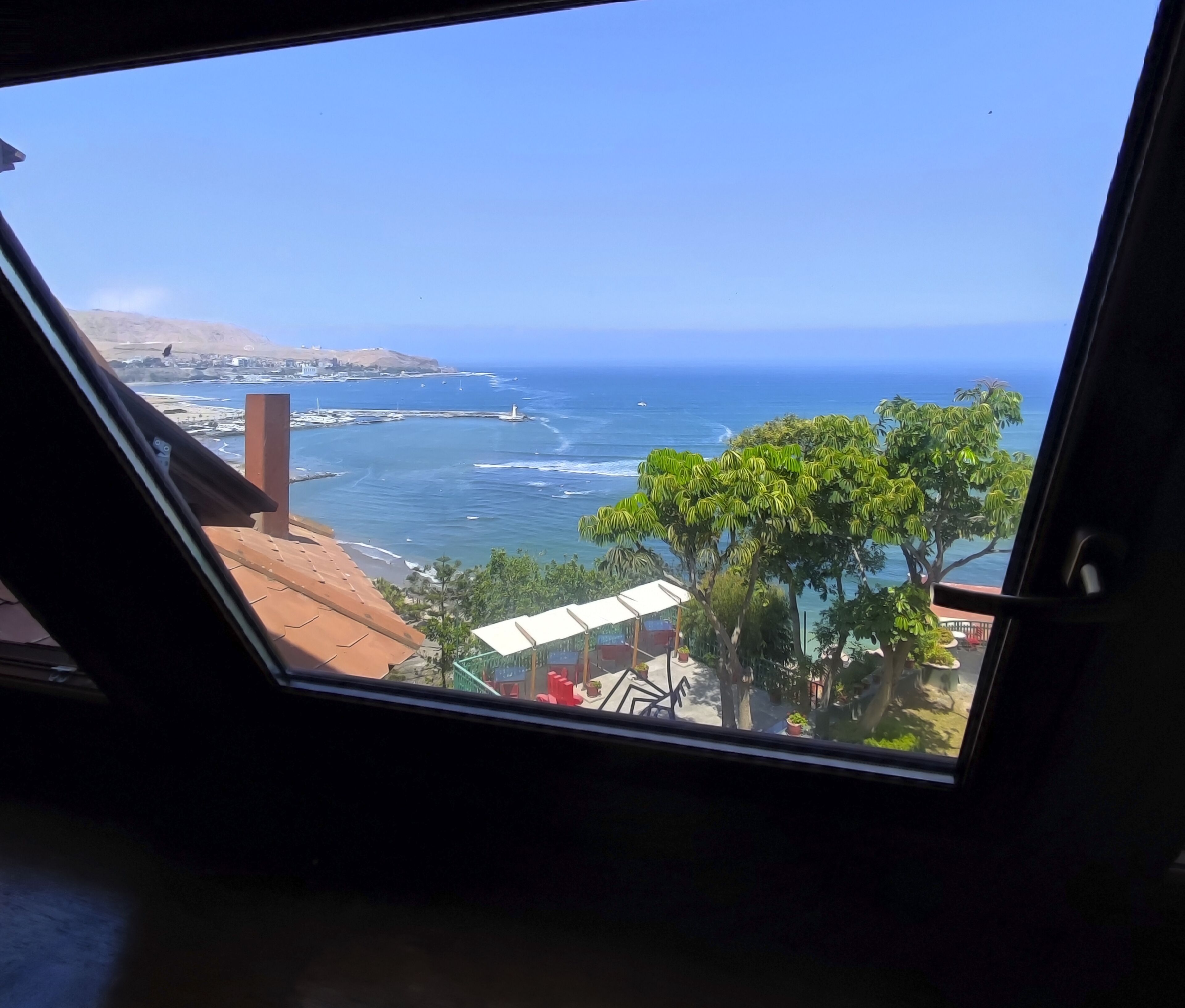 Vista sulla costa da una finestra, con spiaggia, oceano e cielo sereno.