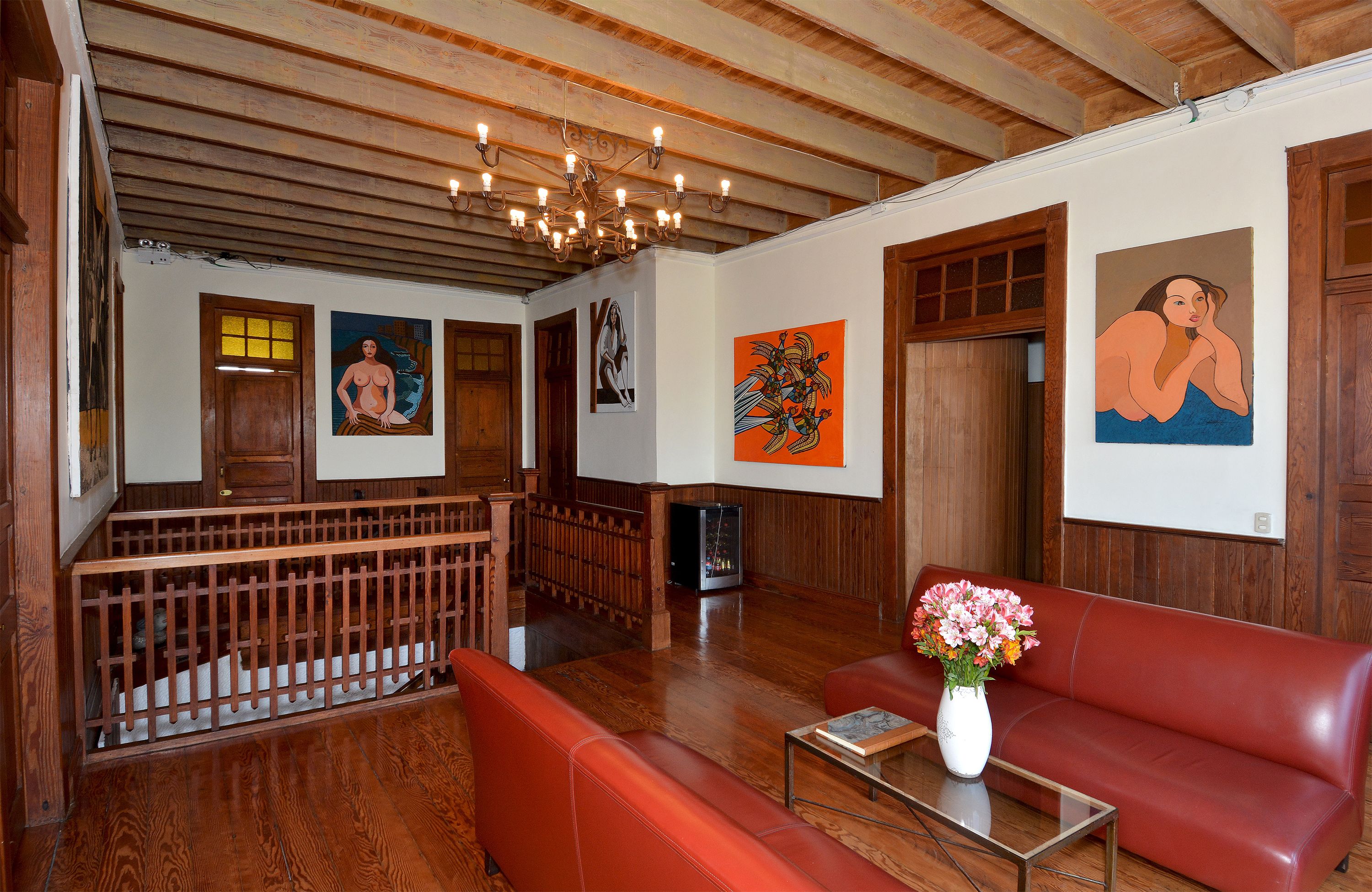 A room with wooden flooring, a red leather sofa, a glass coffee table, and a chandelier.