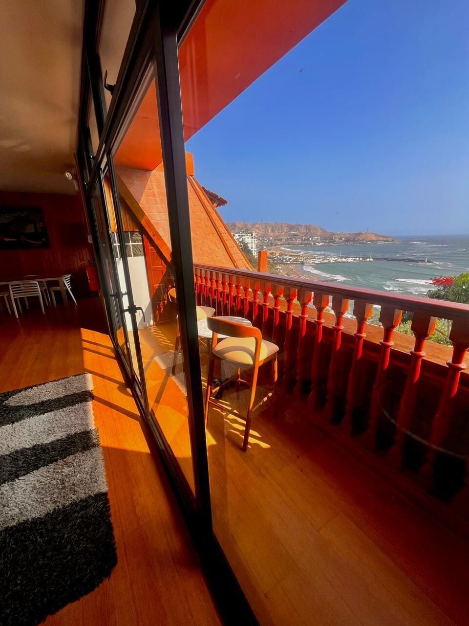 Ein Balkon mit Blick auf den Ozean, Holzboden und ein rotes Geländer.