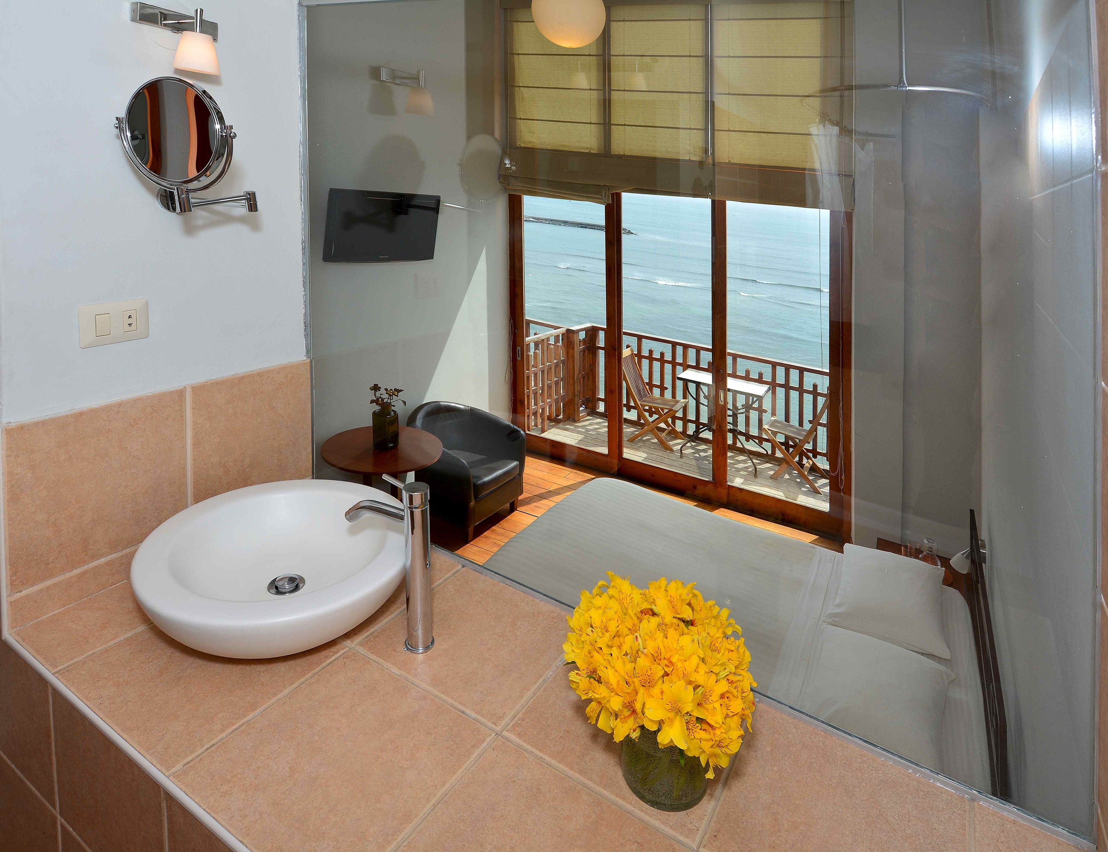 Un baño con lavamanos, espejo y un jarrón de flores amarillas.