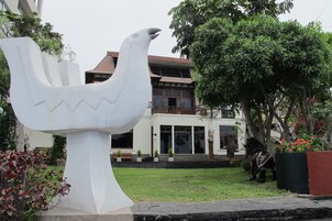 A large white sculpture of a bird in a garden area with a building in the background.