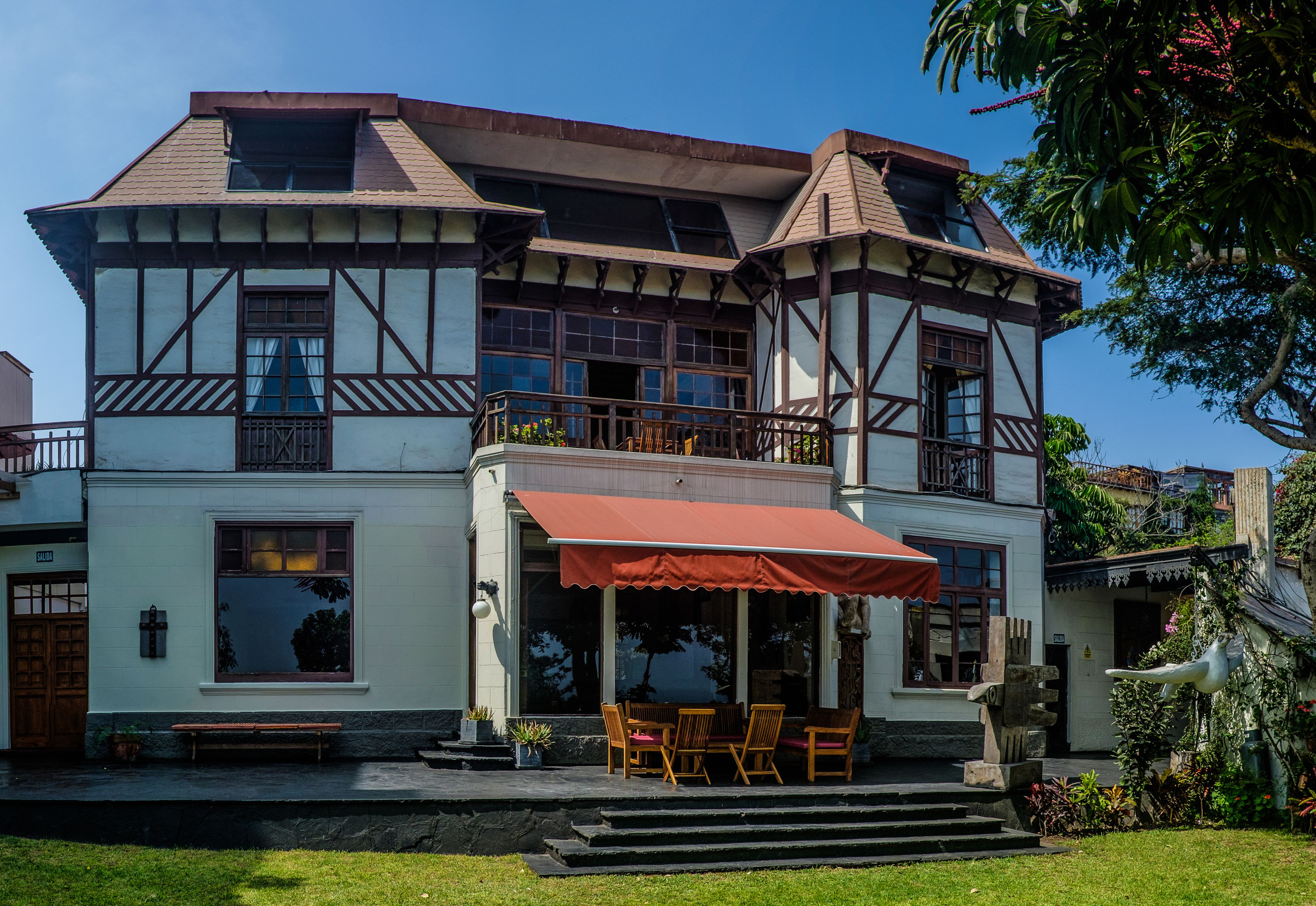 A two-story building with a balcony, a red awning, and a bench outside.