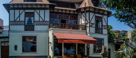 A two-story building with a balcony, a red awning, and a bench outside.