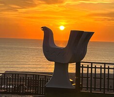 A sculpture of a bird in flight with a sunset in the background.