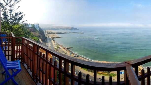 Un balcón con vista a un paisaje urbano costero, que incluye una playa y una carretera que lleva a la ciudad.