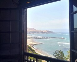 A coastal view from a window, including a beach, ocean, and a distant hill with buildings.
