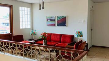 A spacious living room with a red sofa, two wall-mounted lamps, and a decorative railing.
