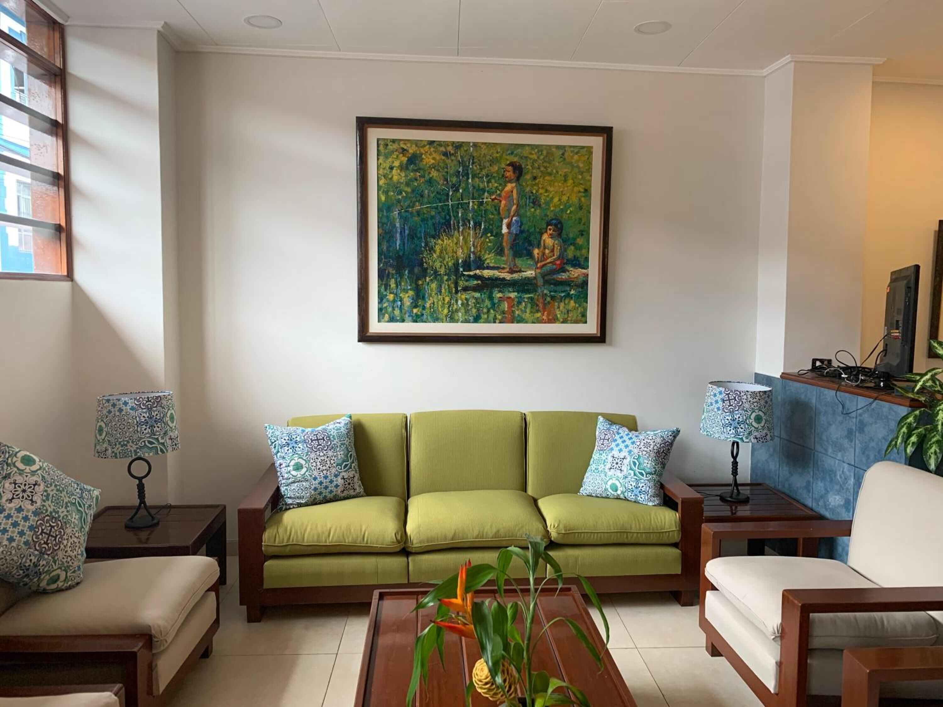 A living room with a green sofa, patterned pillows, a coffee table with a plant, and a painting on the wall.