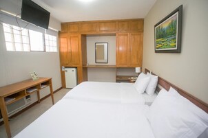 Habitación de hotel con una cama grande, armarios de madera, un escritorio pequeño, un espejo y un cuadro en la pared.