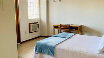 A bedroom with a bed, a desk, a chair, a TV, and a window.