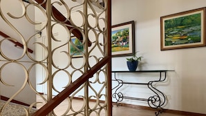 A staircase with a decorative metal railing, a glass table with a potted plant, and two framed paintings on the wall. - Hotel Acosta (Iquitos)